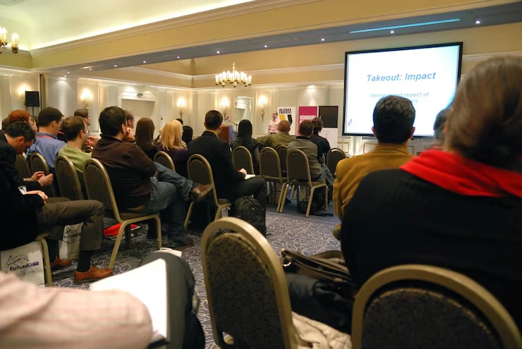 Professional attendees focused on presentation displaying "Takeout: Impact" in elegant hotel conference room