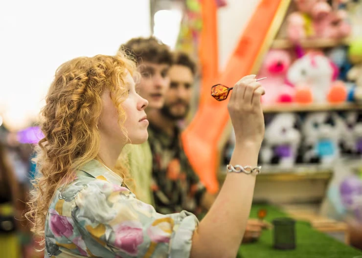 Woman with curly hair painting face design while festival participants watch in colorful marketplace setting