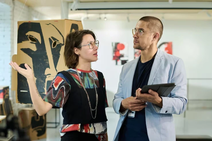 Gallery curator explaining artwork details to visitor using tablet in contemporary art exhibition space