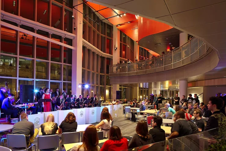 Orchestra performing for seated audience in modern concert hall with curved balconies and dramatic lighting