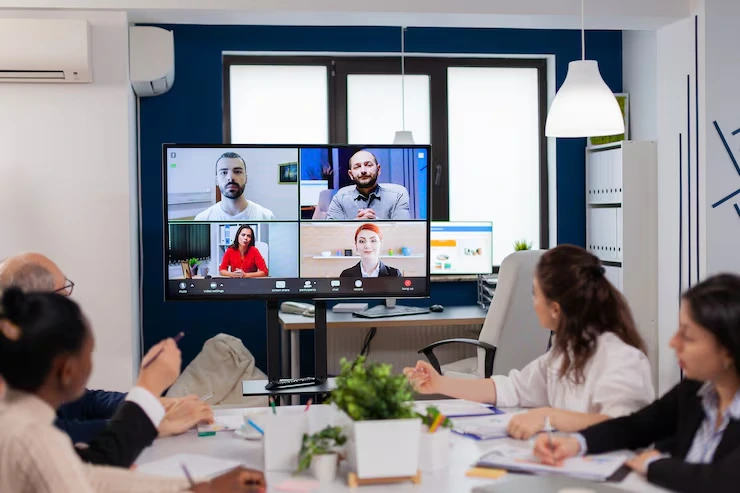 Team attending video conference with four remote participants displayed on large monitor in modern office meeting room