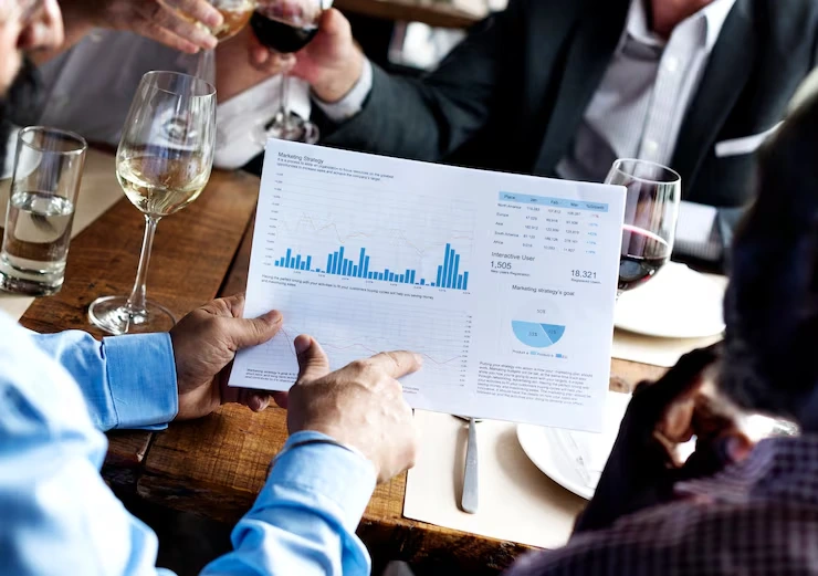 Business executives reviewing detailed analytics charts and graphs during wine reception meeting