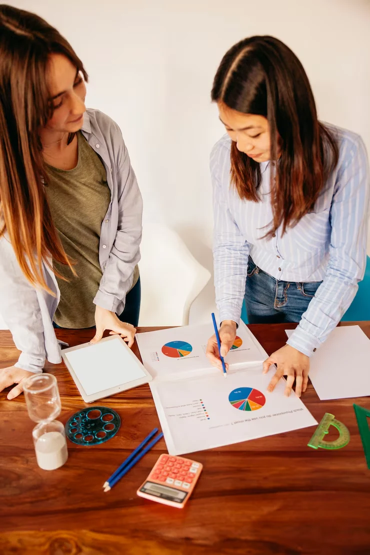 Two analysts reviewing colorful pie charts and event industry data reports on wooden desk with calculator