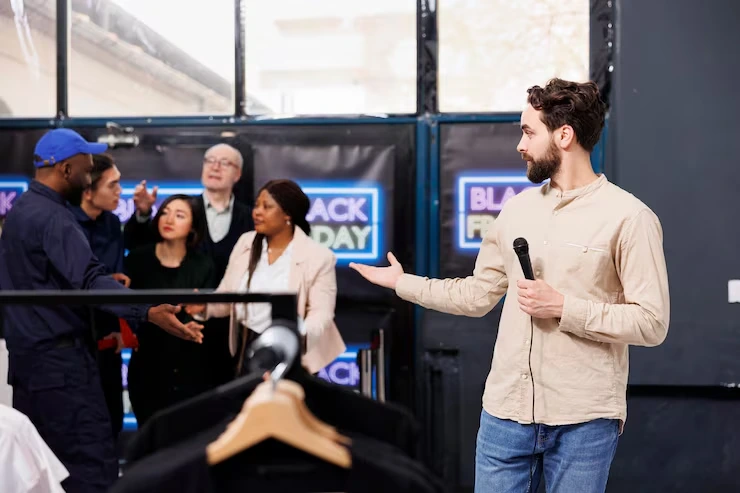 Professional speaker presenting product launch to engaged audience with branded displays and staging