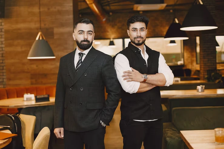 Two professional hospitality staff in formal attire standing confidently in upscale restaurant setting