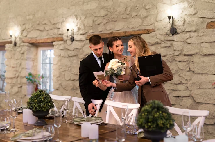 Wedding planner reviewing ceremony details with bride and groom in rustic stone venue with elegant table settings