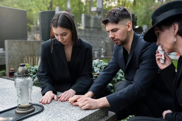 Three mourners in dark suits placing hands together on memorial stone at peaceful cemetery setting