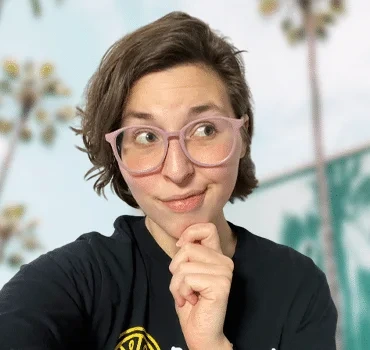 Lydia, operations director, wearing glasses in thoughtful pose outdoors with palm trees behind