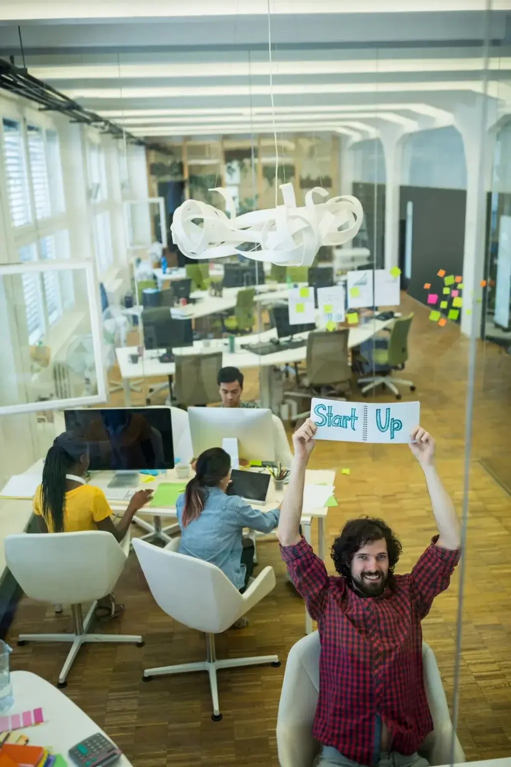 Team member celebrating with startup sign in modern collaborative workspace with colleagues brainstorming