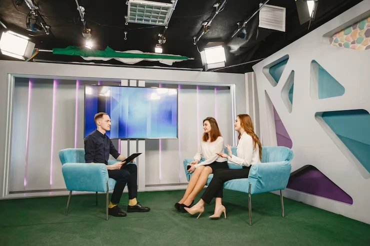 Professional interview setup in modern TV studio with host and two guests seated in turquoise chairs