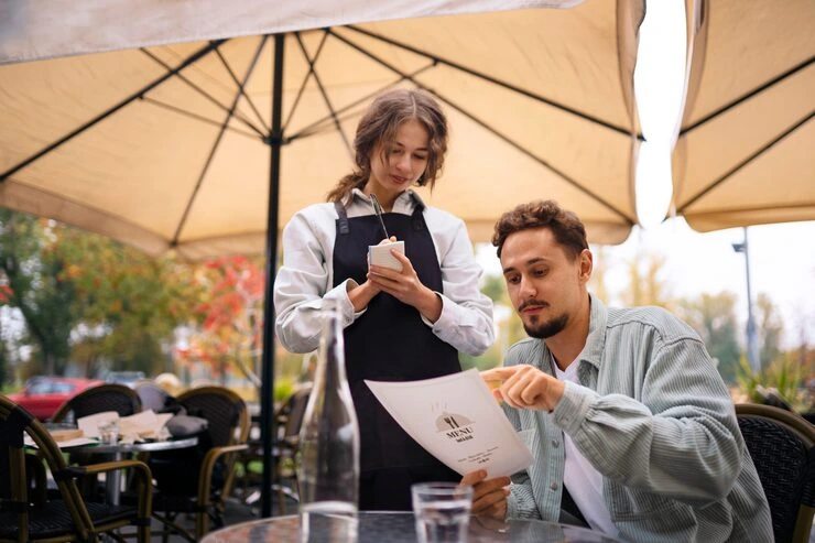 Server taking order from guest at outdoor cafe terrace under umbrella on autumn day