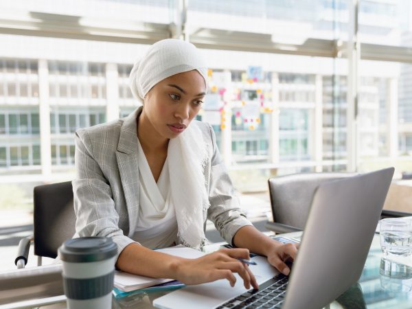 Businesswoman in hijab working on laptop at desk in a modern office