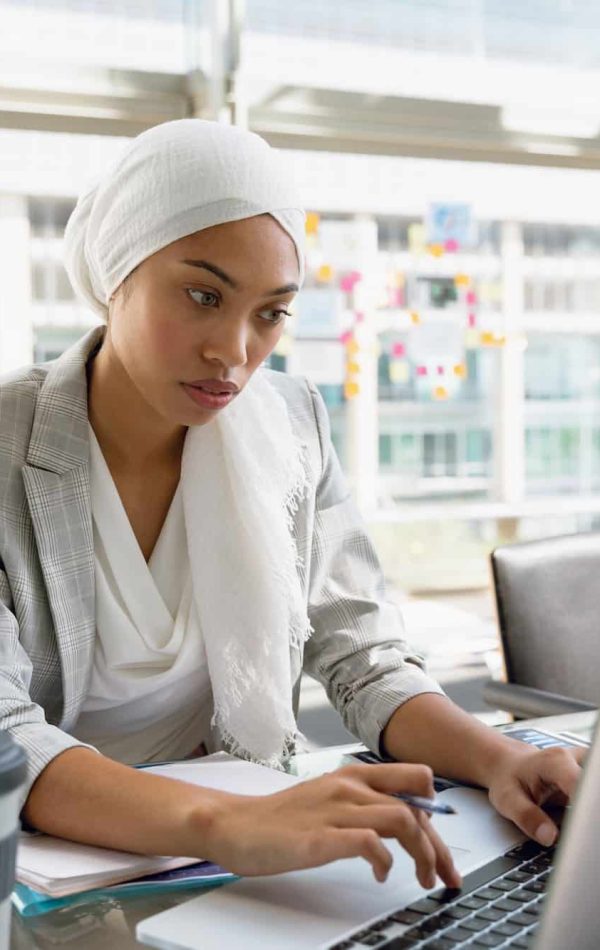 Businesswoman in hijab working on laptop at desk in a modern office, B2b Brand Positioning Agency In London