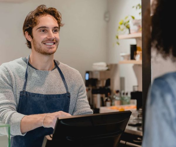 Smiling helpful young waiter servicing the customer at cash point in cafe, Best Creative Agency London